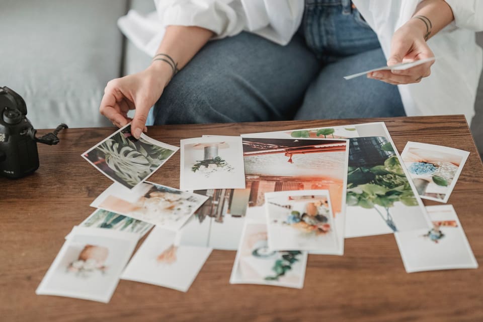 Crop anonymous tattooed female sitting on couch while choosing photos of flowering plants at wooden desk
