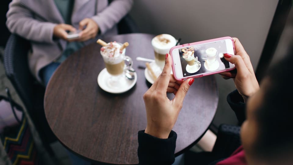 Two women in a cafe capturing photos of their coffee with smartphones.